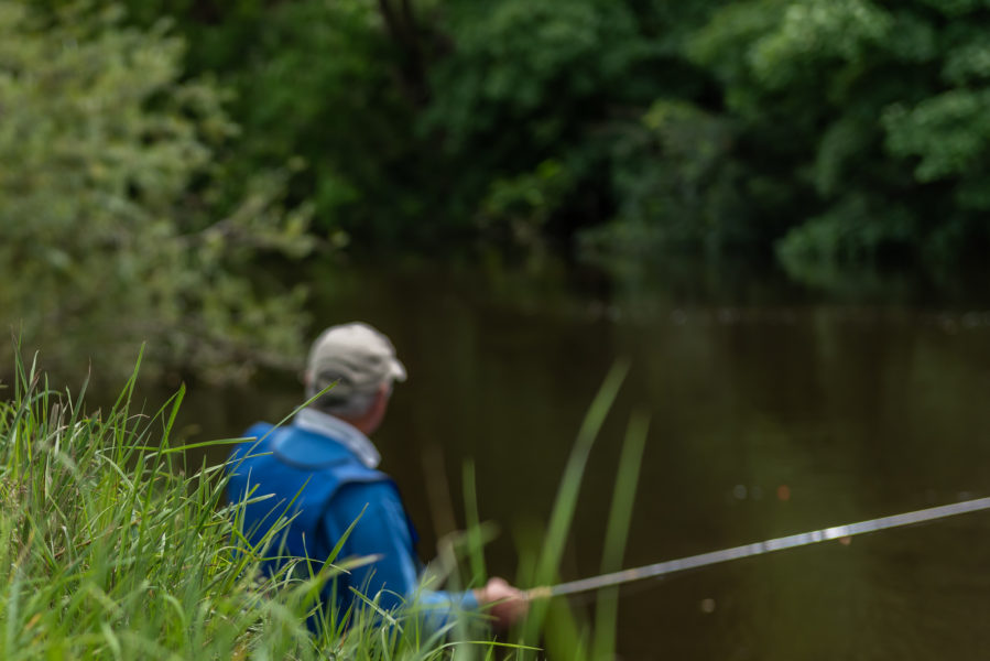 A man in a blue mac fishing in a river